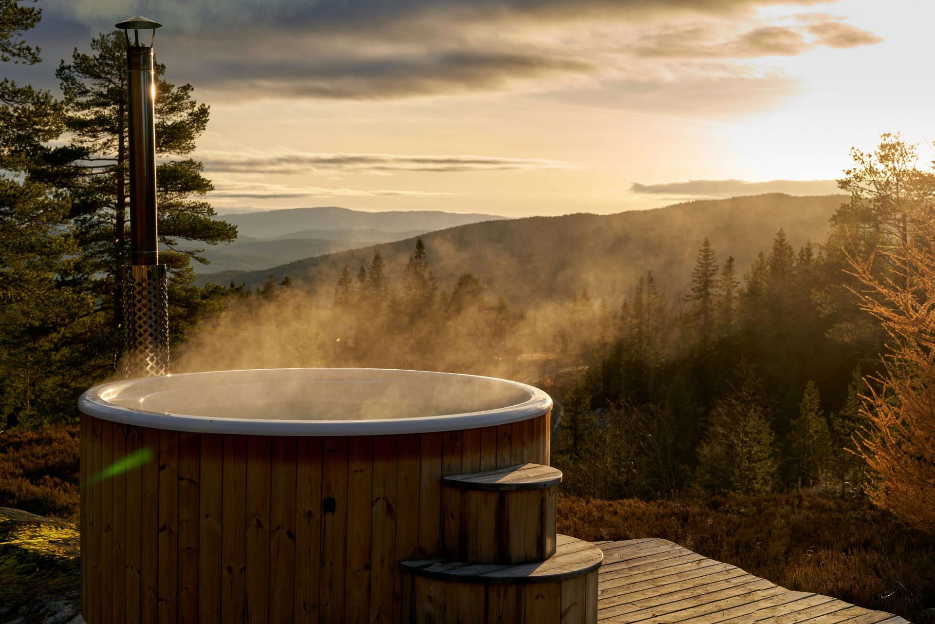 Outdoor Hot Tub aus Holz mit Dampf vor Bergpanorama bei Sonnenuntergang